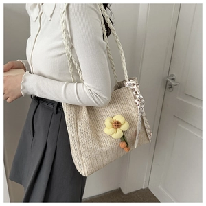 Détail du sac seau en paille beige tissé avec breloque fleurie et ruban sur l'anse