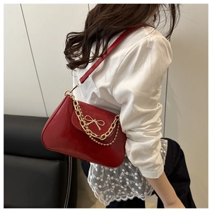 Detail of red glossy leather shoulder bag with gold bow clasp and chain strap