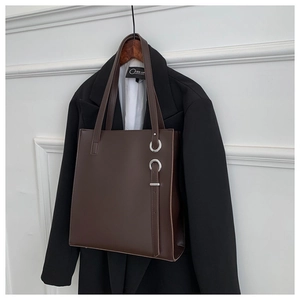 Detail of dark brown leather tote bag with silver metal rings on office suit