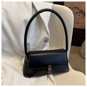 Close-up of black PU leather handbag with vintage bronze metal buckle on a white chair