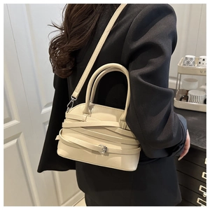 Detail of beige shell bag featuring criss-cross straps and metallic buckles on the side