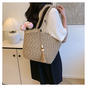 Detail of woven straw tote bag featuring bohemian tassel charm and floral accent decor