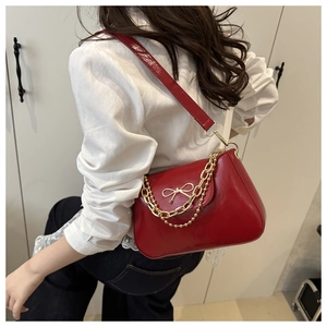 Détail du sac à bandoulière en cuir brillant rouge avec nœud doré et chaîne métal