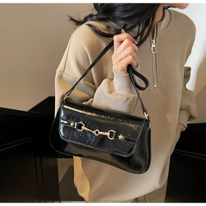 Detail of glossy black leather shoulder bag with gold horsebit buckle on beige sweater