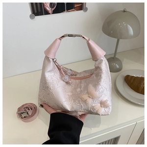 Détail d'un sac à bandoulière en dentelle rose avec broderies papillons et poignée en cuir