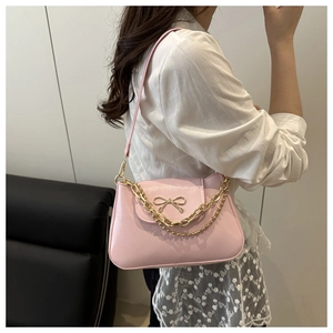 Détail du sac bandoulière en cuir rose avec nœud métallique et fines chaînes dorées