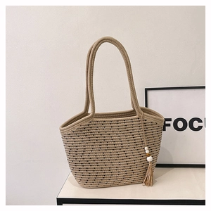 Close-up of beige straw tote bag with black texture, long straps and tassel pendant