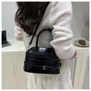 Detail of glossy black shell bag with silver buckles on white sweater background