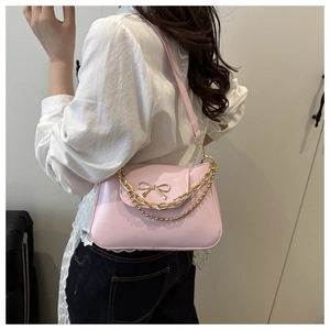 Close-up of pink PU leather baguette bag with golden bow clasp and double chain detail