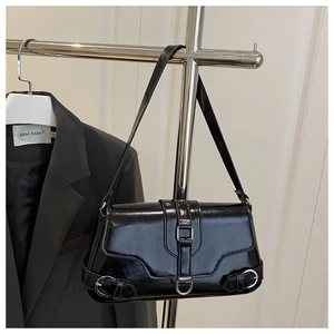Détail du sac à bandoulière en cuir verni noir avec boucle argentée sur fond de blazer