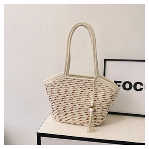 Detailed shot of woven straw tote bag featuring contrast textures and boho tassel charm