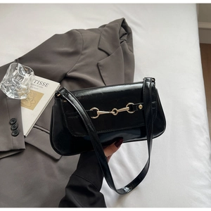 Detail of a black glossy leather shoulder bag with a refined golden horsebit buckle