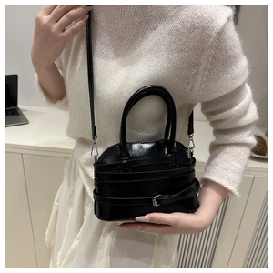 Detailed close-up of glossy black leather shell bag featuring multi-layer strap accents