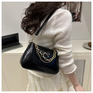 Détail du sac bandoulière en cuir verni noir avec chaîne dorée et boucle nœud élégante