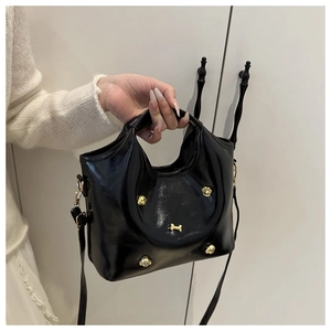 Detail of black glossy handbag featuring gold dog-themed metal rivets and detachable strap