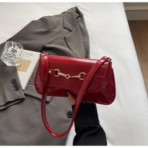 Detail of red patent leather shoulder bag featuring a gold metal horsebit buckle accessory