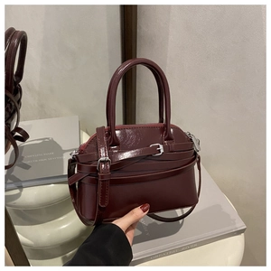 Close-up of burgundy patent leather handbag with layered straps and silver hardware detail