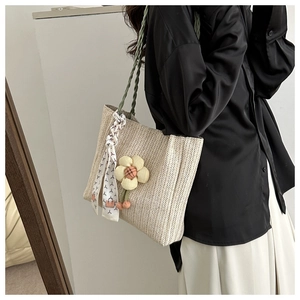 Détail d'un sac cabas en paille tressée avec poignées vertes, foulard et breloque tournesol