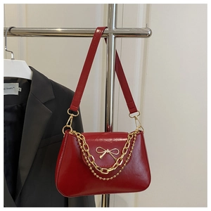 Detail view of red patent leather baguette bag with golden bow clasp and metal chain
