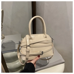 Detailed view of beige shell handbag showing decorative straps and metal buckle accents
