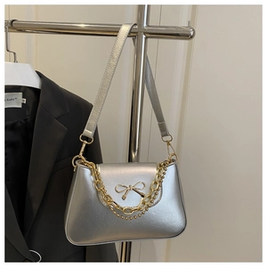 Detail of silver shoulder bag featuring a metallic bow and gold chain decoration