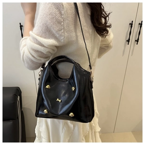 Detail of black glossy bucket bag with golden dog charm on white knit outfit