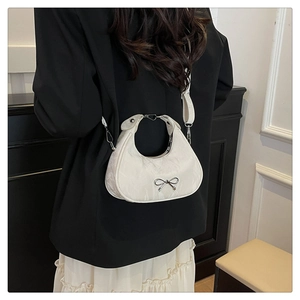 Detail of white crescent bag with silver bow accent on model wearing a black blazer