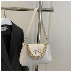 Detail of white glossy shoulder bag with golden bow buckle and double metal chains