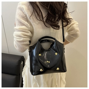 Detail of black glossy tote bag with heart stitching and gold puppy charms on model