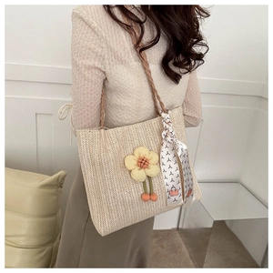 Détail du sac seau en paille avec motif floral et foulard en soie sur la poignée