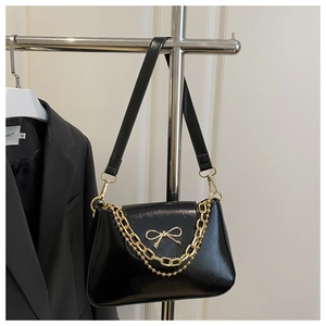 Detail of black glossy shoulder bag with golden bow and double decorative chains