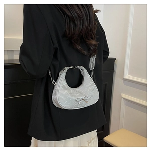 Detail of light grey crescent bag with bow decoration shown on model's shoulder