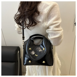 Detail of glossy black tote bag with gold poodle studs and adjustable shoulder strap