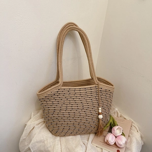Minimalist straw tote bag with black polka dots and decorative tassel on a white table