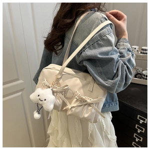Detail of cream canvas underarm bag featuring bow pockets and a cloud plush pendant