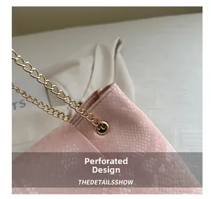 Close-up of pink faux lizard texture leather bag with gold chain and perforated design