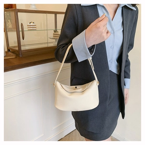Close-up of cream lychee pattern leather handbag with gold buckle on office outfit