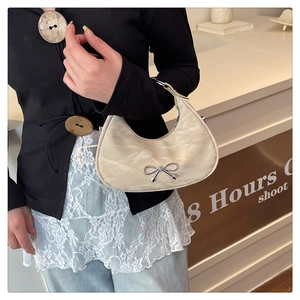 Detailed view of cream crescent bag featuring cloud pleats and a silver metal bow