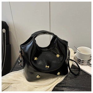 Detail of black patent leather bag featuring golden puppy and bone charms on white silk