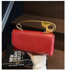 Macro detail of the red glossy leather texture and signature gold safety pin handle