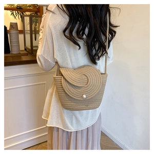 Close-up of woven straw crossbody bag with pearl buckle and textured round flap detail