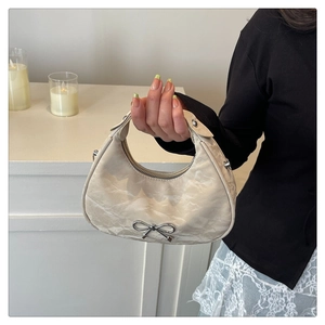 Gros plan du sac hobo en tissu crème texturé avec détail de nœud argenté élégant