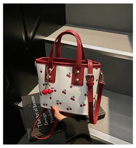 Detail of white cherry print mini tote bag with red leather trim and matching cherry charm