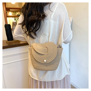 Detail of beige straw woven crossbody bag with pearl button closure on female model