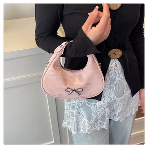 Détail d'un sac demi-lune en satin rose avec nœud métallique porté par un mannequin