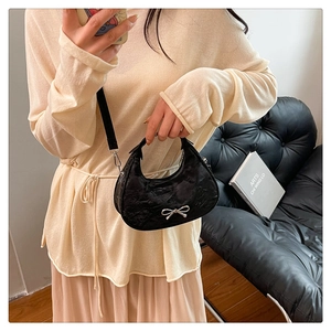Detailed view of black pleated crescent bag with a silver bow clasp worn by a model