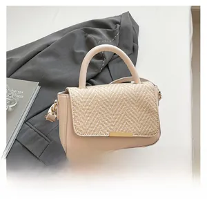 Detail of beige contrast handbag featuring woven texture flap and gold metal clasp
