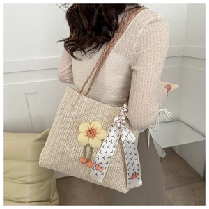Détail d'un sac seau en paille tressée avec breloque fleurie et poignée en soie décorée