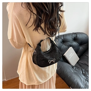 Detail of black crescent shoulder bag with silver bow ornament and pleated texture finish