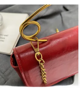 Detail of red wax leather crossbody bag with iconic gold safety pin hardware and chain